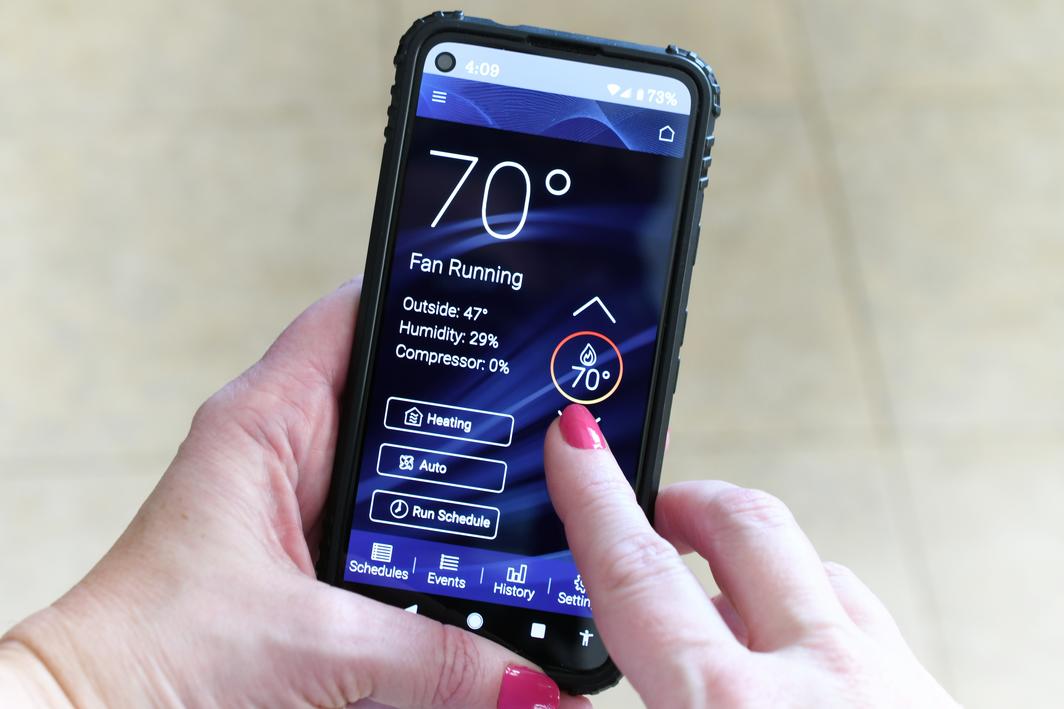 A woman with pink painted nails, holding a mobile phone device while changing home temp from her smart thermostat application.