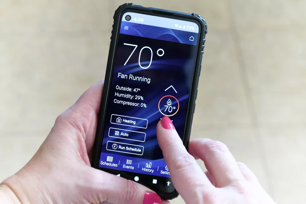 A woman with pink painted nails, holding a mobile phone device while changing home temp from her smart thermostat application.