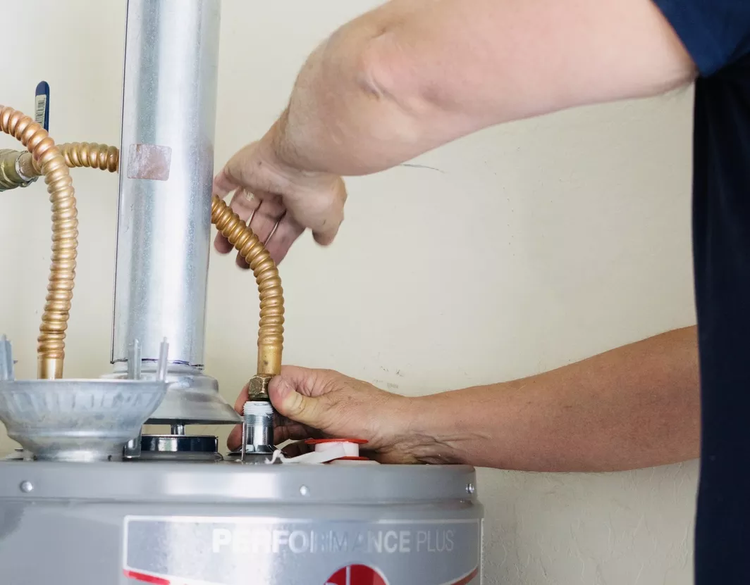 Technician working on the outside connections to the top of a water heater.