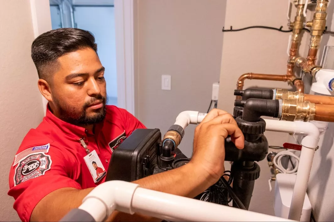 Uniformed Jon Wayne tech working on a water softener system installed inside a home.
