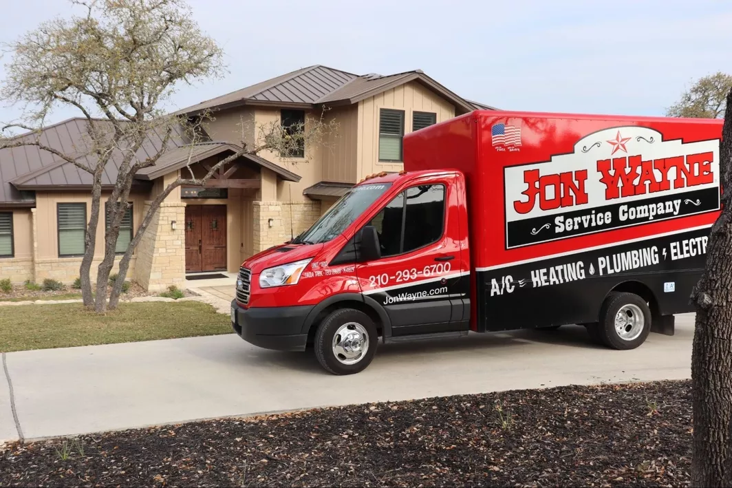 A branded Jon Wayne service truck parked in the driveway of a two story home.