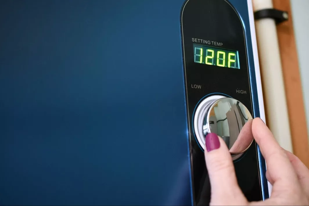 A right hand turning the temperature dial on a tankless water heater, showing a setting temp of 120F.