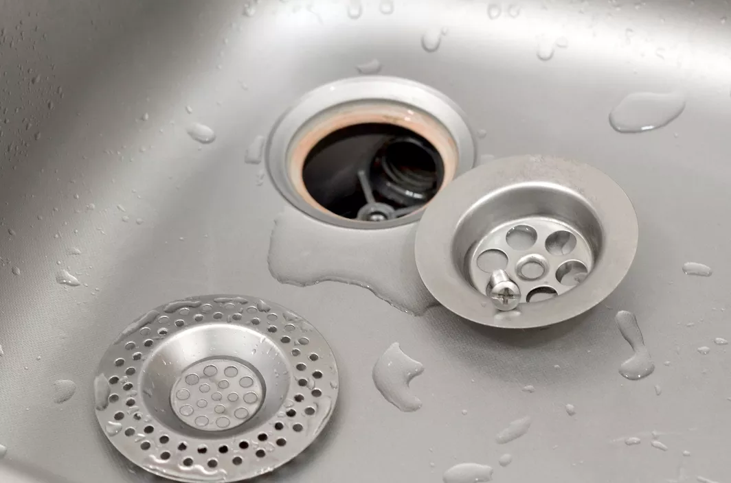 A closeup of an open drain in a stainless steel sink with water droplets inside