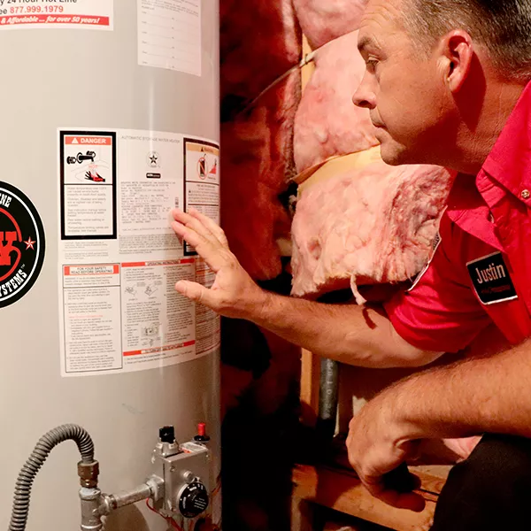 Uniformed Jon Wayne tech inspecting a water heater that is installed near a wall that has pink insulation.